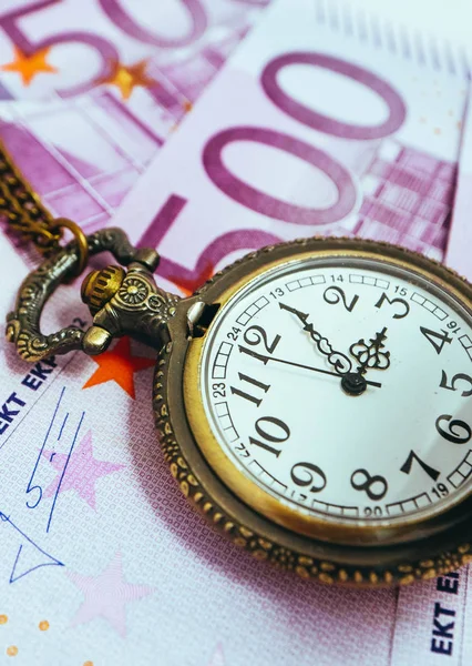 Old pocket watch with euro banknotes money, macro view. Time and business concept.