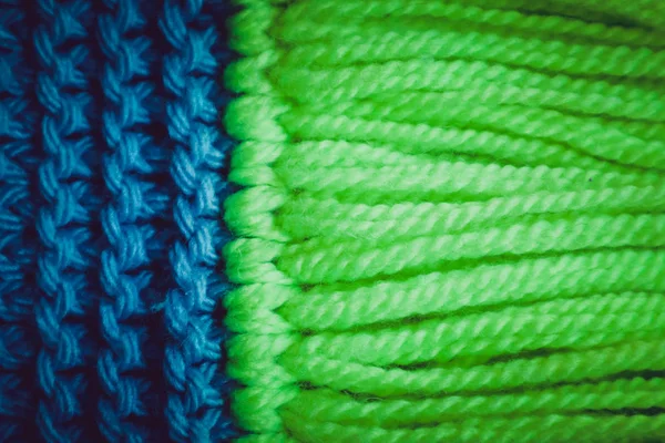 Knitwear woolen textile texture backdrop, macro. Blue and green color palette clothes, scarf tassels.