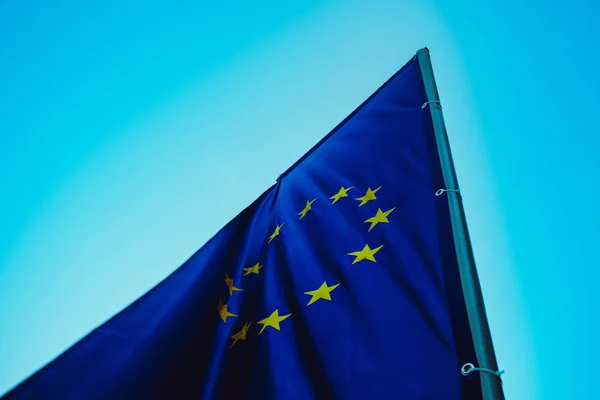 European union flag, blue sky on the background. Blue European union flag with yellow stars in a circle waving on wind.  Macro view, close up.