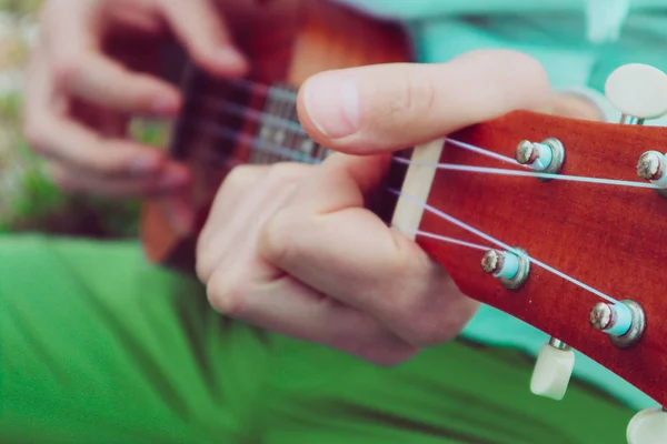 Photo depicts musical instrument ukulele guitar in the hands of player. Musician fingers are playing on the small ukulele guitar. Strings close up, macro view.