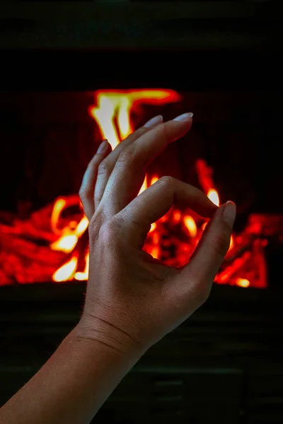 A woman hand warming up near the fireplace. Ok hand gesture, fire flame on the background.