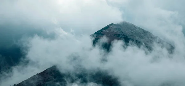 Beautiful foggy mystic mountain peak. Mystical autumn landscape, hills in a fog clouds. Europe, mysterious alpine landscape.