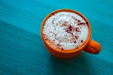 Kapuçino üzerinde deniz mavi ahşap masa kahve büyük bir turuncu bardak.