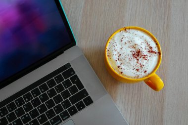 Cappuccino kahve ofis ahşap masa üzerinde laptop klavye arka planda büyük bir sarı bardak.