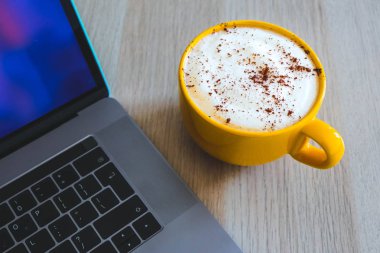 Cappuccino kahve ofis ahşap masa üzerinde laptop klavye arka planda büyük bir sarı bardak.