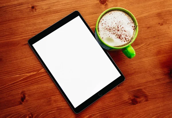 Cappuccino kahve ofis ahşap masaları ve bir ipad tablet mockup boş ekran ile büyük bir yeşil bardak.