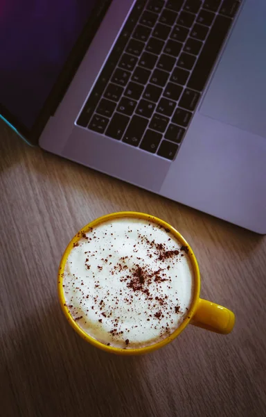 Cappuccino kahve ofis ahşap masa üzerinde laptop klavye arka planda büyük bir sarı bardak.