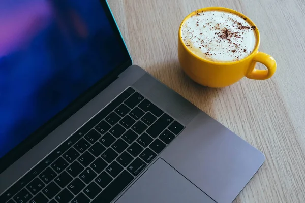 Cappuccino kahve ofis ahşap masa üzerinde laptop klavye arka planda büyük bir sarı bardak.