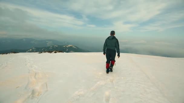 O homem está se movendo ao longo do topo da montanha coberta de neve — Vídeo de Stock