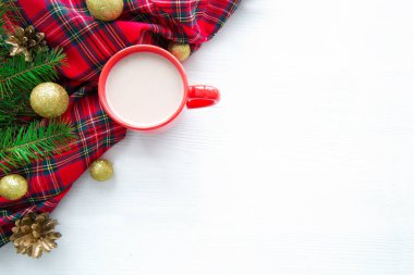 Beyaz ahşap masada kırmızı bir fincan sıcak çikolata. Klasik ekose ve altın Noel topları.. 