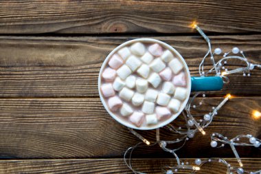 Kahverengi ahşap masa üzerinde lokum bulunan lezzetli sıcak çikolata, sarı Noel ışıkları. Metin için boşluk, kopyala boşluk. 