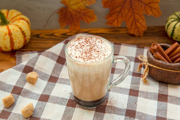 Pumpkin coffee with spices, dried leaves and little pumpkins, warm autumn colors.