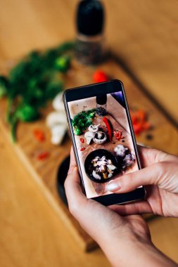 Kadın, mussele, kırmızı biber, taze yeşillikler, mantarlar, üzerinde çekici kadın elleri olan brokoli ve ahşap bir masa üzerindeki kırmızı biber gibi yiyeceklerin fotoğrafını çekiyor.