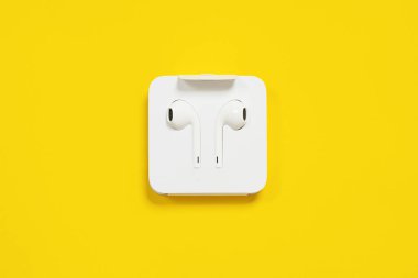 01 Mayıs 2020, Rostov, Rusya: Karton fabrika ambalajında beyaz tel Earpod 'lar, parlak sarı arka planda. Metin veya reklam için kapatma, izole etme, kopyalama alanı.