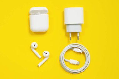 01 Mayıs 2020, Rostov, Rusya: Apple cihazları seti, beyaz kablosuz hava podları, sarı zemin üzerinde C tipi elektrik prizi ve kablo yıldırımı. Boşluğu kopyala, kapat.