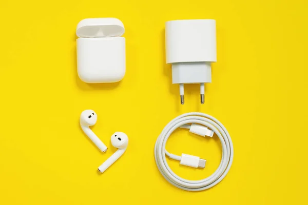 01 de mayo 2020, Rostov, Rusia: Conjunto de dispositivos Apple, AirPods inalámbricos blancos con caja, enchufe de alimentación y relámpago de alambre a usb tipo c, sobre fondo amarillo. Copiar espacio, primer plano . — Foto de Stock