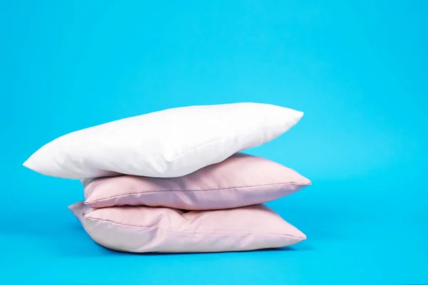 Three pillows stacked on top of each other, white and pink color, on bright blue background. Bed linen and bedding, housekeeping. Copy space. — Stock Photo, Image