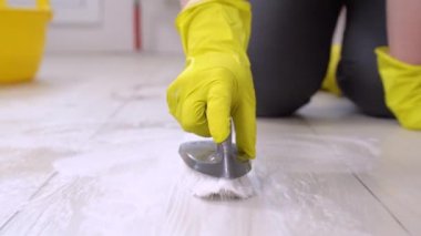Sarı lastik eldivenli, su dolu plastik bir leğen, köpüklü deterjan ve yerdeki fayansları fırçalayan bir kadın. Yüzeylerin dezenfekte edilmesi, genel temizlik..