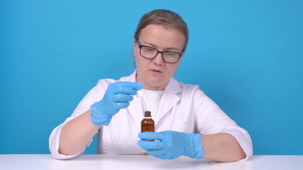 Блондинка в медичному пальто, стерильні захисні силіконові рукавички і окуляри акуратно вимірює необхідну дозу крапель ліків з піпеткою за рецептом лікарів . — стокове відео