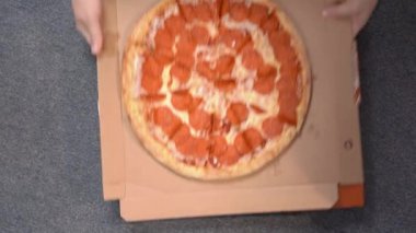 Adam, baharatlı sosis dilimleri ve erimiş peynirle dolu bir pizza kutusunu halı yüzeyine koyar, yaramaz dachshund köpeğini mavi tişörtlü çalar ve gizlice yer, üstten görünür.