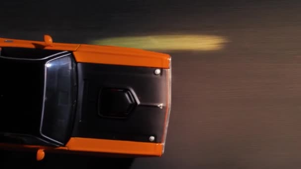 Julio 14, 2020, Rostov, Rusia: Cool sport orange toy car Dodge Challenger 1970 lanzamiento va rápido, se mueve alrededor, evitando obstáculos en la carretera, faros iluminan el camino, vista desde arriba, de cerca. — Vídeo de stock