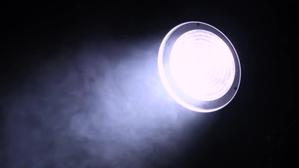 Light of cars headlight or stage spotlight glows in the dark, mysterious and ominous smoke slowly hovers around, night shooting, close up. — Stock Video