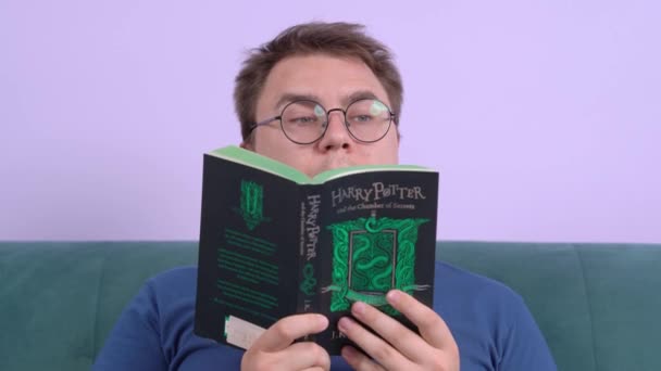 Rostov, Rusia 20 de julio de 2020: Retrato de un joven hombre leyendo la novela Harry Potter y la Cámara de los Secretos, sosteniendo el libro en ambas manos. Mira algo y sacude la cabeza negativamente. — Vídeo de stock