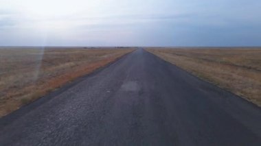 Köyde hasat edilen ekinlerle birlikte tarımsal tarlaların ortasında terk edilmiş bir yolda hızla uçan bir insansız hava aracı vurmak. Terk edilmiş vahşi bölgelerde seyahat edin.