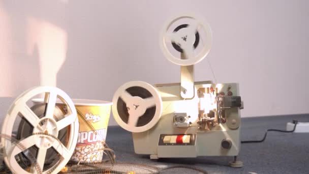 El viejo proyector de película retro está funcionando y mostrando películas, la bombilla es brillante y los carretes giran. Cubo de palomitas de caramelo o saladas para ver cine nocturno en compañía de amigos — Vídeos de Stock