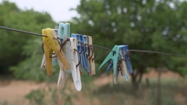Stare plastikowe szpilki wiszą na linie do tradycyjnego sposobu suszenia prania na wsi, huśtawka na wietrze, zbliżenie, zamazane tło z drzewami. Małe rzeczy do pomocy gospodyniom domowym w pracy — Wideo stockowe