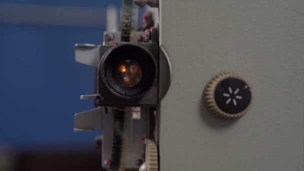 Bulb lights up inside device and shines through lens of movie projector, front view, close up. Person turns handle to adjust desired mode. Configuration and maintenance of old equipment. — Stock Video