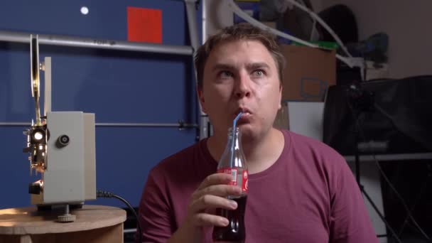 Rostov, Rosja, 01 sierpnia 2020: Emocjonalny człowiek ogląda fascynujący film używając starego projektora filmowego z rolkami. Facet je pizzę z kawałkami pikantnej kiełbasy i pije sodę przez słomkę ze szklanej butelki. — Wideo stockowe