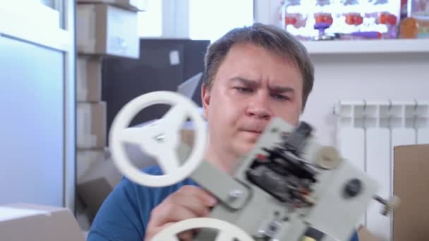 Le jeune homme est occupé à trier les ordures à la maison. Guy trouve vieux bobine-à-bobine film projecteur vintage et sourit nostalgiquement à ses souvenirs, hoche la tête — Video