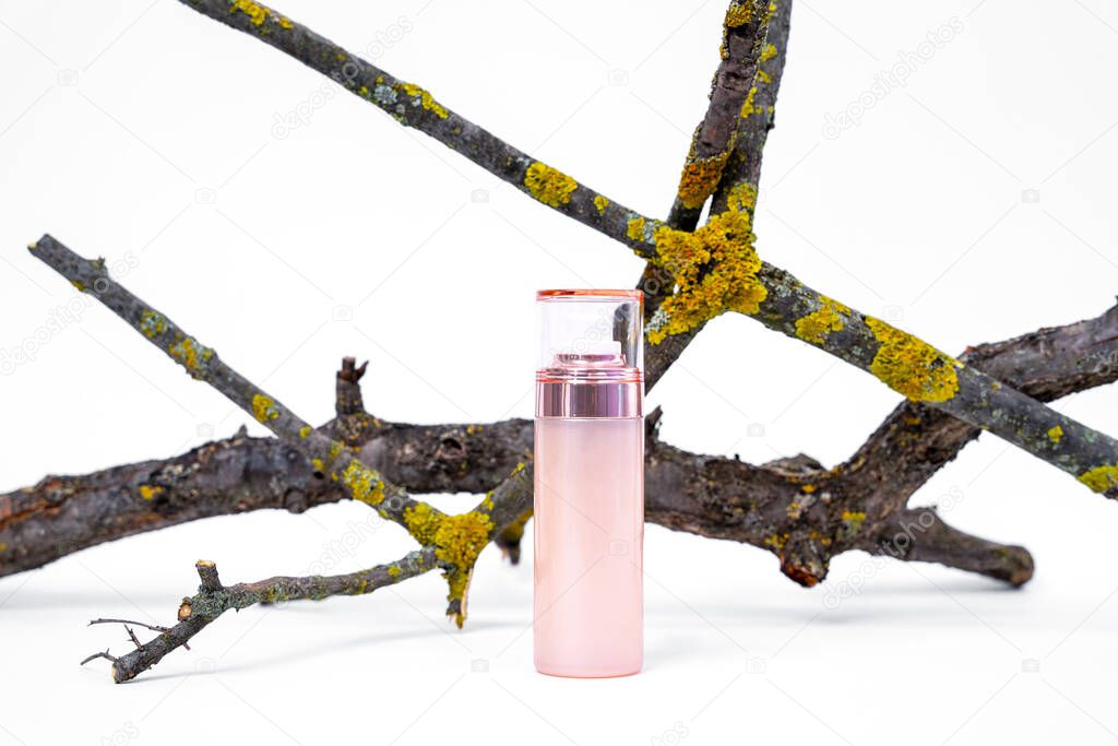 Creative advertising of cosmetic product containing natural ingredients in beautiful bottle with dispenser and cap on white background, dry branches covered with moss for decoration, copy space