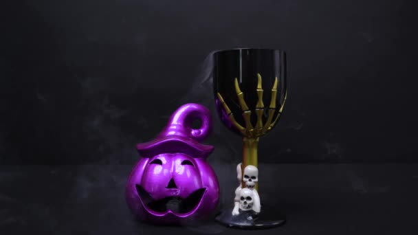 Griezelige glimlachende paarse jack lantaarn pompoen en rokerige beker gevuld met giftige toverdrank versierd met schedels en skelet hand voor Halloween feest op zwarte achtergrond — Stockvideo