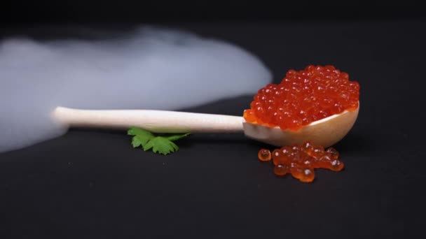 Fantastisk lyx presentation av del av röd lax kaviar ligger i handgjorda träsked, svart bakgrund. Moln av tjock rök rulla över välsmakande lyx delikatess nationella ryska köket. — Stockvideo