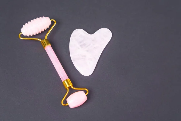 Double-sided dermatology roller made of rose quartz and gua sha scraper for rejuvenating and wellness massage of face, neck and decollete area on black background, top view, copy space — Stock Photo, Image