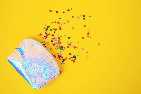 Creative composition with shiny multicolored plastic and glass gems and beads spilled out from leather cosmetic bag of mother-of-pearl color, top view, copy space for advertisement