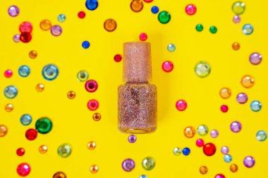 Şişenin üst görüntüsünü pembe ojeli gümüş ya da parlak sarı arka planda çok renkli pullar ve yapay jemlerle kapat.