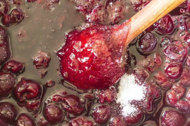 Kiraz reçeli pişirme. Bir tahta kaşıkla karıştırın sıcak koyu kırmızı kiraz ve beyaz şeker. Meyve, meyveler, yiyecek, mutfak ve pişirme hakkında bir sitedir.