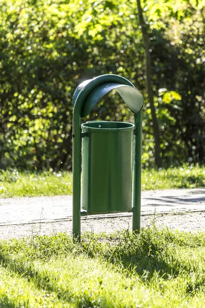 Güneşli bir bahar günü. Döşeli patika Parkı sokak yeşil metal çöp kutusu. Taze yeşil çim ve yeşillik. Site hakkında parklar, doğa, mevsim.