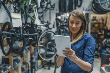 İşyerinde kadın makinist. Tablet bir bisiklet tamir ederken kullanma. Kadın Bisiklet Bisiklet dükkanında dijital tablet kullanarak teknisyen onarın. Denetim listesini doğrulayın. Mekanik kadın bir şey bir tablet pc ve denetim listesi denetleme.