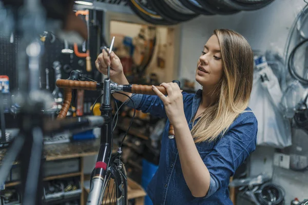 女自行车修理工正在车间修自行车 技师妇女修自行车在修理店 调整自行车链和修理自行车的年轻妇女 自行车服务 — 图库照片
