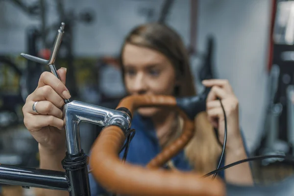 Woman bike mechanic working on bicycle. Young woman master is fixing wheel of city-bike in bicycle service. Technical expertise taking care Bicycle Shop