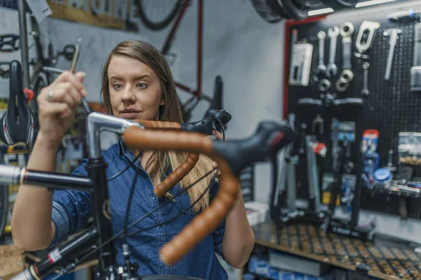 Woman bike mechanic working on bicycle. Young woman master is fixing wheel of city-bike in bicycle service. Technical expertise taking care Bicycle Shop