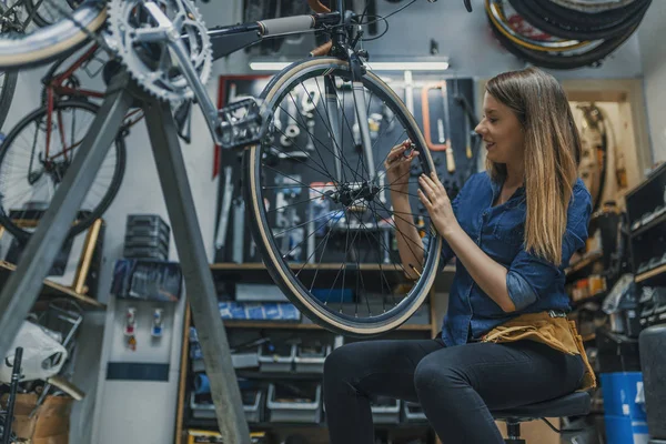 自行车服务 Servicewoman 修理工安装或调整车轮上的自行车齿轮车间 在自行车修理店工作的年轻妇女 — 图库照片