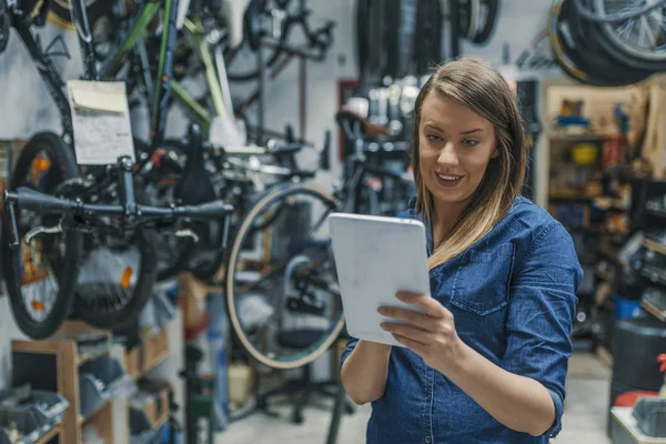 Female mechanic at work. Using a tablet while fixing a bicycle. Female bicycle repair technician using digital tablet in bicycle shop. Verify the checklist. Mechanic woman checking something on a tablet-pc and checklist.