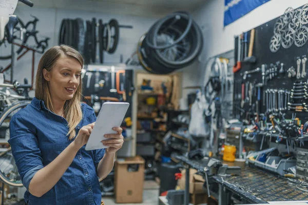 İşyerinde kadın makinist. Tablet bir bisiklet tamir ederken kullanma. Kadın Bisiklet Bisiklet dükkanında dijital tablet kullanarak teknisyen onarın. Denetim listesini doğrulayın. Mekanik kadın bir şey bir tablet pc ve denetim listesi denetleme.