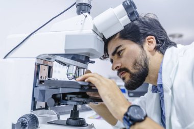 Laboratuvar mikroskop ile genç öğrenci araştırmacı adam çalışın. Yakışıklı adam onun laboratuvar mikroskop çalışırken cam slayt örnekleri inceleyerek. Erkek bir bilimsel araştırmacı Close-up