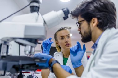 Çekici genç bilim adamı ve onun sonrası doktora danışmanı mikroskop slayt arıyorum. Genç kadın araştırma bilim adamı ve hazırlama ve mikroskop slaytlar araştırma laboratuarında analiz erkek şefliği.